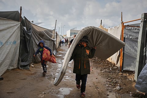 Salam Musa, 9, carries a mattress as he walks between tents after rainfall at a temporary camp in Deir al-Balah, in the central Gaza Strip, on Friday, Nov 14, 2025.