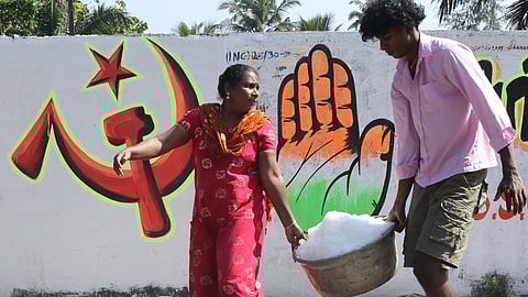 : Fish workers carry a tub of ice past poll graffiti of two rival parties sharing the same wall at Anchuthengu in Thiruvananthapuram on Thursday, reflecting the vibrant yet competitive atmosphere as campaign activity picks up across Kerala ahead of the local body elections
