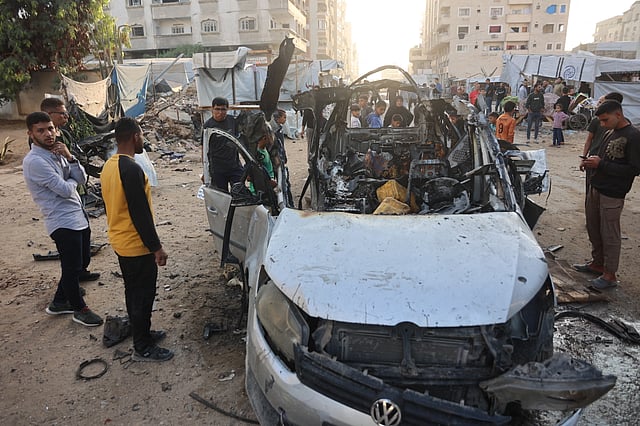Palestinians, some displaced, gather to look at a destroyed vehicle targeted by the Israeli military, in Gaza City on November 22, 2025.