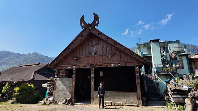 Kevi, a young tour guide in Khonoma Village, poses in front of the morung, a traditional youth dormitory that serves as a center for education for young Naga men