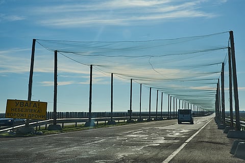 A car drives on a road covered with an anti-FPV-drone net, a road sign reading "Attention/Danger/Enemy drones", at the approaches to the frontline city of Kherson, Southern Ukraine, Sunday, Nov. 2, 2025.