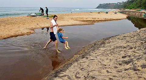 A tourist hauls his daughter out of the dirty, stinking stream of contaminated water flowing on the beach. 