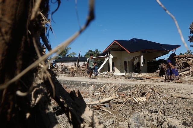 People walk past the ruins of houses at a village affected by flood in Batang Toru, North Sumatra, Indonesia, Wednesday, Dec. 3, 2025. 
