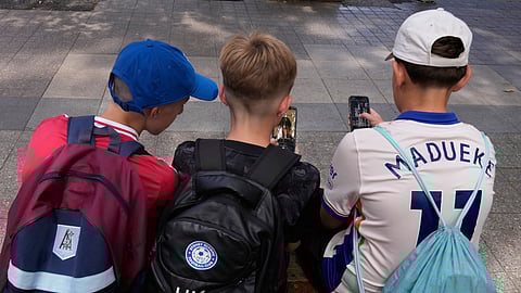 Hugo Winwood-Smith, right, Hardy Macpherson and Edan Abou, left, all 11 years old, use their phones while sitting outside a school in Sydney on Monday, Dec. 8, 2025.