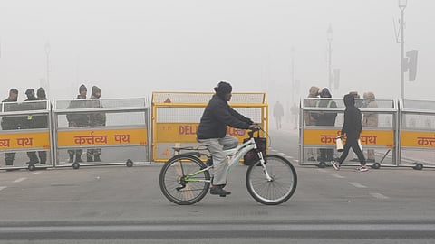 A cyclist passes by security barricades along a fog-covered Kartavya Path on a cold winter morning, in New Delhi, Monday, Dec. 15, 2025