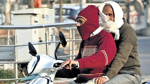 A man rides a scooter wearing a sweater and balaclava while the pillion rider uses a scarf to ward off the cold in Karimnagar