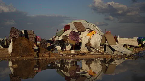 A tent is reflected in water at a makeshift camp for displaced Palestinians where a woman washes clothes on the beach in Gaza City, Tuesday, Dec. 16, 2025.