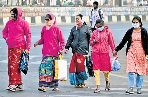 Women walk across a road wearing warm clothing to beat the morning chill at Karimnagar.