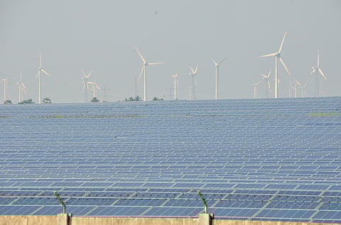Solar panels spread across a vast field with windmills standing in the background at Manur in Tirunelveli distri