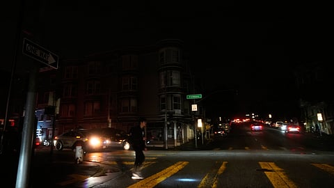 A pedestrian uses a flash light while crossing an intersection as power outages darken the streets, in San Francisco, Saturday, Dec. 20, 2025.