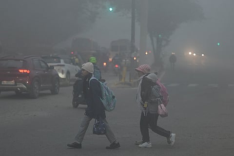 People walk along a road amid dense fog, affecting visibility on a winter morning, in New Delhi.
