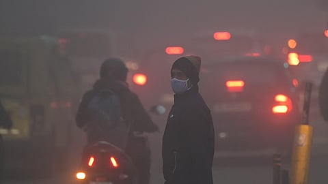 People walk along a road amid dense fog, affecting visibility on a winter morning, in New Delhi on Monday.