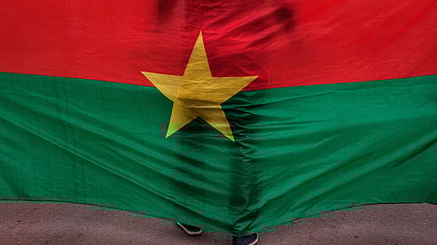 The Burkina Faso national flag with a man standing in front of it is seen during a memorial ceremony in Ouagadougou, Burkina Faso, Jan. 23, 2016. 
