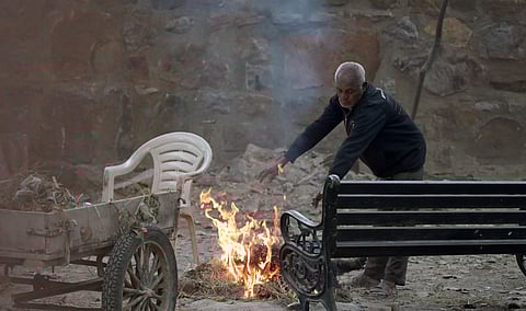 A man sit around a bonfire to warm themselves on a cold winter afternoon in New Delhi on Thursday.