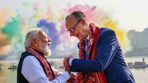 Prime Minister Narendra Modi greets German Chancellor Friedrich Merz as they share a light moment against the backdrop of colourful smoke trails released over the Sabarmati river during the International Kite Festival, in Ahmedabad.