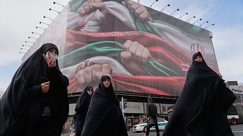 Women cross a street under a huge banner showing hands firmly holding Iranian flags as a sign of patriotism in Tehran, Iran, Jan. 14, 2026.