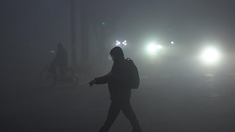 People walk along a road amid dense fog, affecting visibility on a winter morning, in New Delhi