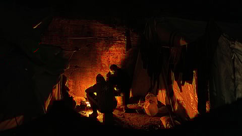 Displaced Palestinians cook and warm themselves around a fire at a tent camp in Gaza City, Sunday, Jan. 18, 2026.