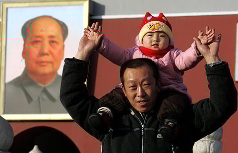 A Chinese man lifts his child onto his shoulders as they pose for a picture in front of a portrait of late communist leader Mao Zedong in Beijing, China.