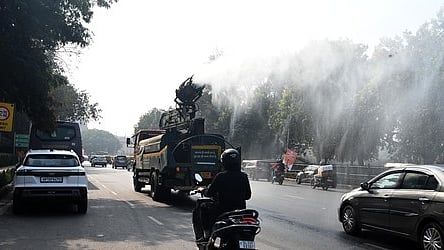 Commuters ride past an anti-smog gun spraying water to curb air pollution amid heavy smog conditions in New Delhi.