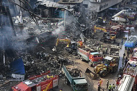 Rescue workers and firefighters work with heavy machinery to search through the rubble of a burnt building of a multistory shopping plaza following a massive fire in Karachi, Pakistan, Monday, Jan. 19, 2026. 