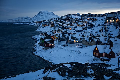 Houses along the coastline are lit as early morning light breaks over the snow-covered hills in Nuuk, Greenland.
