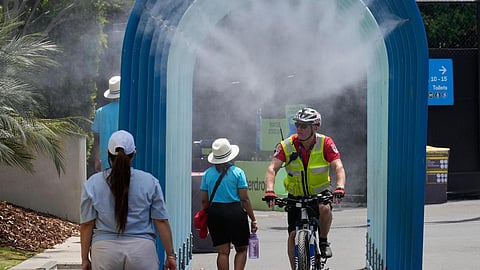 Fans walk and ride bikes through a water mister at the Australian Open tennis championship in Melbourne, on January 27, 2026 