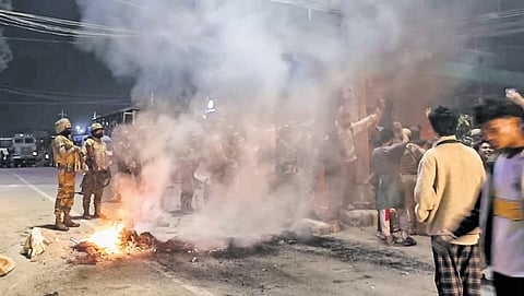 Security personnel keep watch as people stage a protest against the participation of Kuki-Zo MLAs in state government formation in Churachandpur on Thursday.