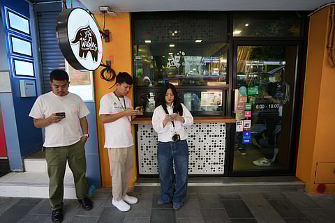 Customers wait for their coffee outside a coffee shop in Bangkok
