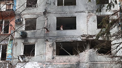 A woman looks out of a broken window after a Russian drone hit an apartment building in Zaporizhzhia, Ukraine, Thursday, Feb. 26, 2026. 