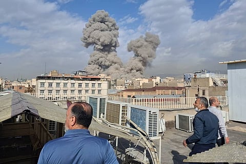 People watch as smoke rises on the skyline after an explosion in Tehran.