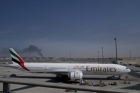 A plume of smoke caused by an Iranian strike is seen in the background as an Emirates plane is parked at the Dubai International Airport after its closure.