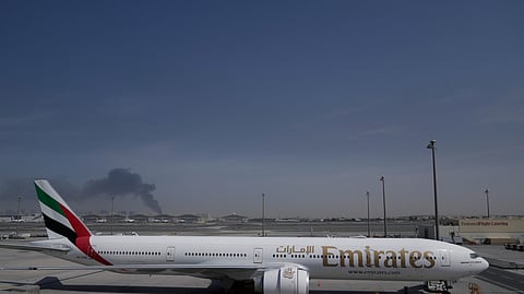 A plume of smoke caused by an Iranian strike is seen in the background an an Emirates plane is parked at the Dubai International Airport after its closure in Dubai, United Arab Emirates, Sunday, March 1, 2026.