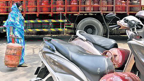 A woman carries an LPG cylinder past two-wheelers amid concerns over a looming cooking gas shortage in Hyderabad on Tuesday.