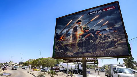 A billboard depicting Ayatollah Ali Khamenei, Iran's late supreme leader who was killed on February 28 in a US-Israeli strike in Tehran, standing behind an Iranian soldier with a caption in Arabic reading "a martyr leads the battlefield" is displayed along a road in the Ameriyah neighbourhood in western Baghdad on March 18, 2026.