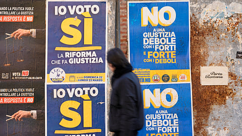 A man passes next to election posters as Italian citizens will be called on March 22th and 23th to approve or reject the constitutional reform of the judicial system introduced by the Meloni government, through a referendum that does not require a minimum voter turnout, in Milan, Italy, Friday, March 20, 2026.