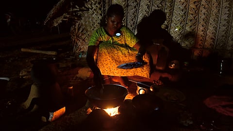 A woman holds a torch between her neck and shoulder while cooking.