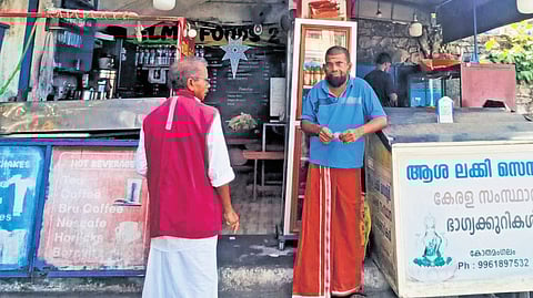 Tea stall owner Jagadish discussing politics, development with a lottery vendor near Kothamangalam