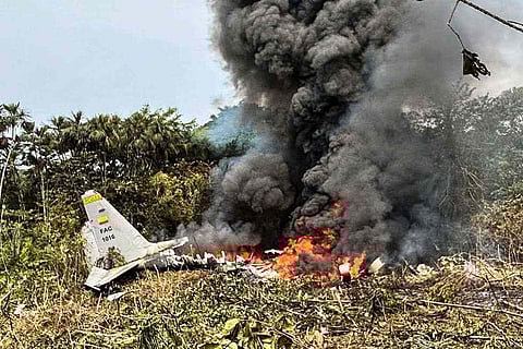 Flames and thick black smoke rise from an Air Force Hercules that crashed during takeoff, as a member of the Colombian Police stands nearby, in Puerto Leguizamo, Colombia, near the southern border with Ecuador, on March 23, 2026.