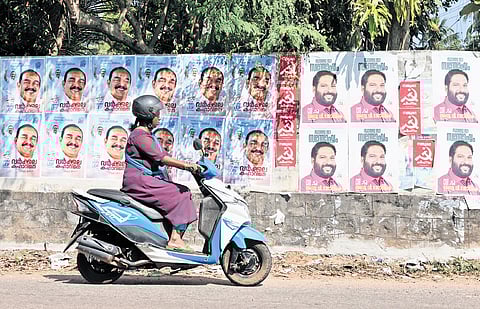 A woman rides past a wall covered with poll campaign posters at Mylamoodu, near Varkala 