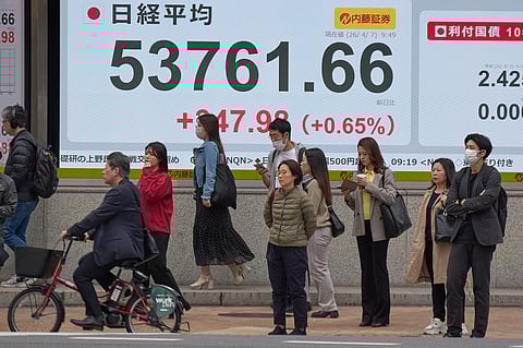 People stand in front of an electronic stock board showing Japan's Nikkei index at a securities firm Tuesday, April 7, 2026, in Tokyo. 