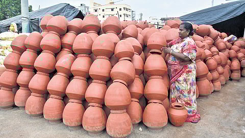 A woman sells earthen water pots on the roadside while another.