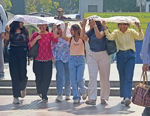 Students use scarves to shield themselves from the sun as temperatures rise in Delhi near Palika Bazaar on Wednesday