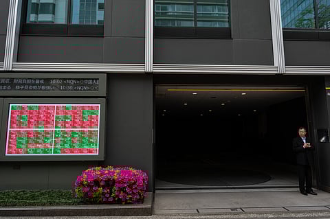 A man stands outside a parking garage next to a stocks display near the Tokyo Stock Exchange in Tokyo on April 20, 2026.