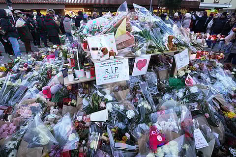 People stand around floral trbutes and candles placed outside the sealed off Le Constellation bar in Crans-Montana, Swizz Alps, Switzerland, on Jan 3, 2026, where a devastating fire left dead and injured during the New Year's celebrations.