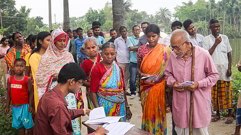 A poll official checks the names of the voters on a list as they wait in a queue to cast their votes in the first phase of West Bengal Assembly elections, at a polling station, in Dakshin Dinajpur district, Thursday, April 23, 2026. 