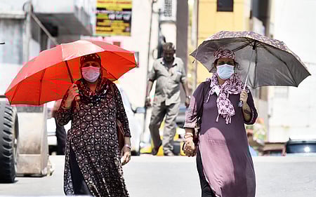 Women use portable shade under an umbrella while navigating the city streets during an intense afternoon heatwave.
