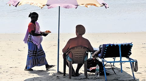 A local vendor offers a plate of freshly cut fruits to a tourist unwinding on Kovalam beach in Thiruvananthapuram.