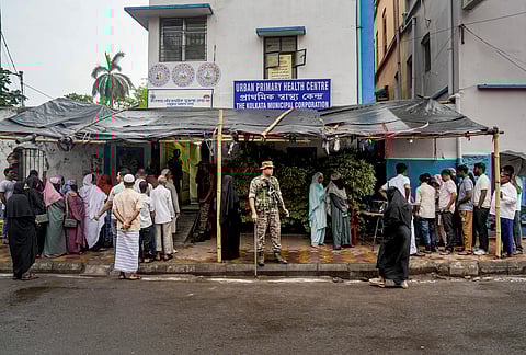 A security personnel stands guard as voters wait in queues to cast their votes during the second and final phase of the West Bengal Assembly elections, at a polling station, in Kolkata, Tuesday, April 29, 2026. 