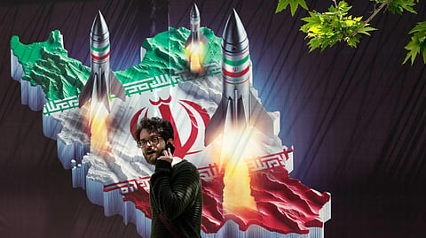 A passerby, taking his cellphone, walks past a banner showing missiles being launched from an Iranian map in northern Tehran, Iran, Friday, April 19, 2024.